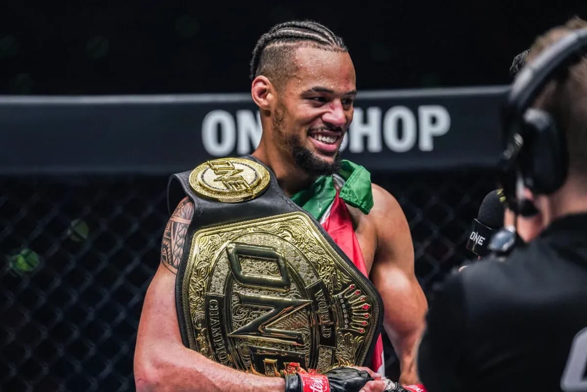 Muay Thai fighter Regian Eersel smiles and poses with the ONE Championship belt in the cage