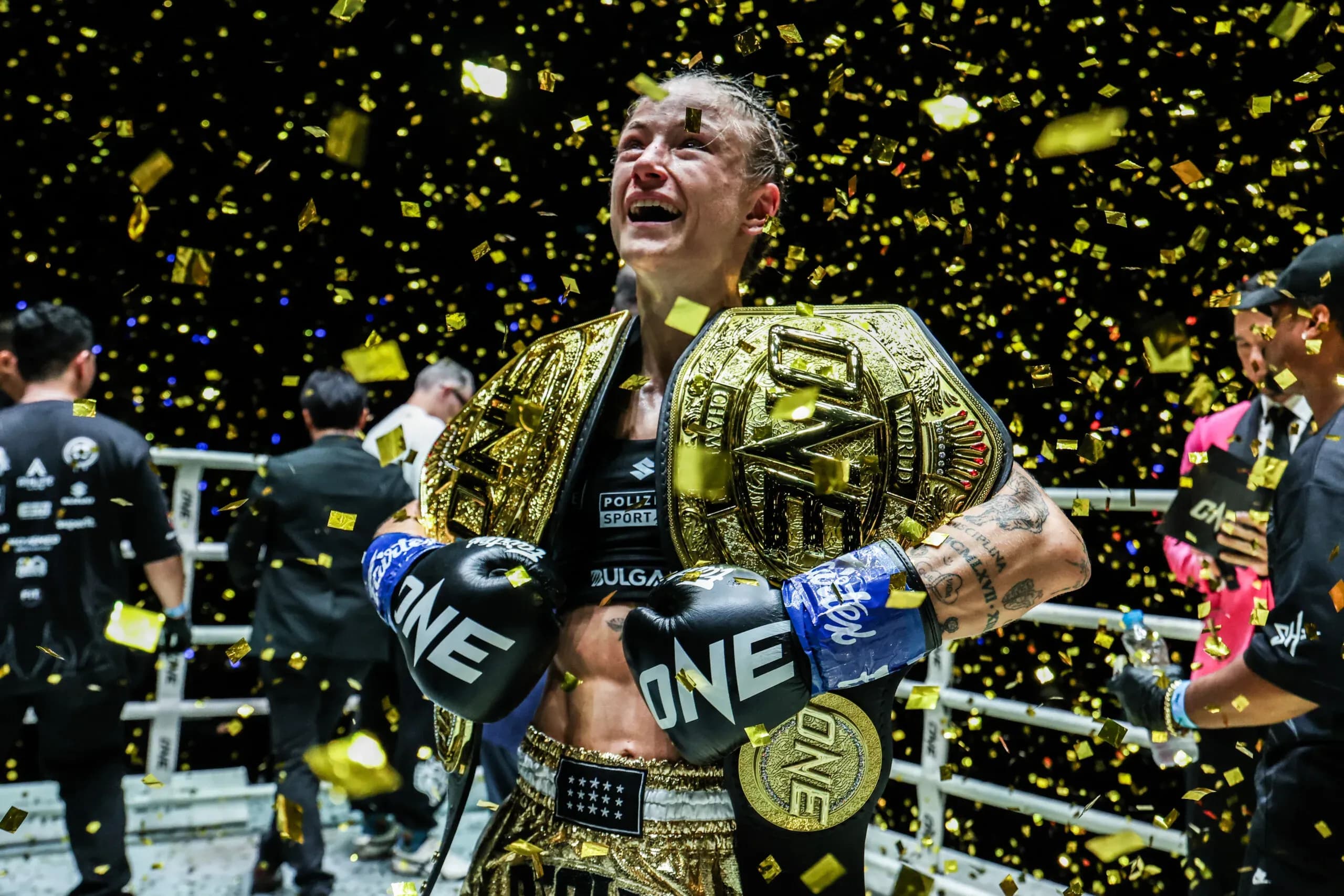 Stella Hemetsberger stands in the ring with two ONE Championship belts over her shoulders